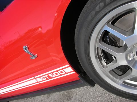 1998 Ford Crown Victoria - Detail of a red Shelby's lower fender showing the GT500 stripe graphic, a chrome cobra badge and a polished wheel.
