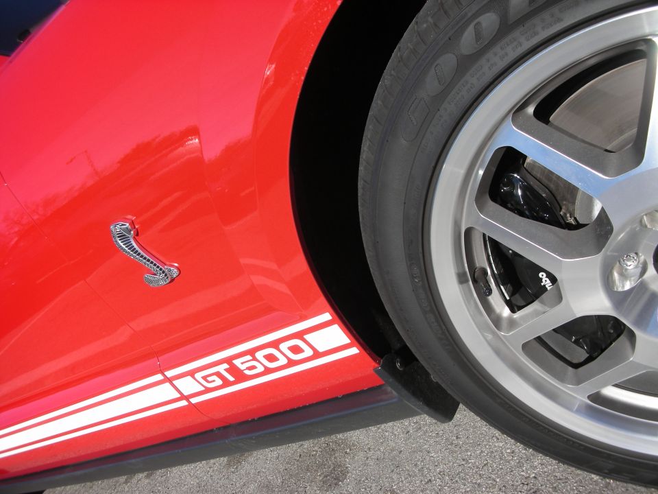 Close-up of red car fender with GT500 stripe, cobra emblem and polished wheel