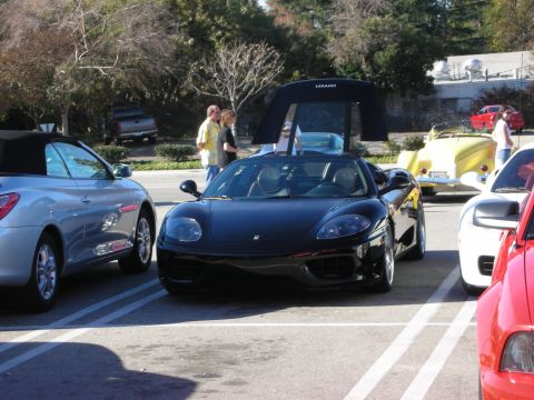 1998 Ford Crown Victoria - black Ferrari 360-series convertible with top stowed sits in a parking space flanked by other cars at a meet.