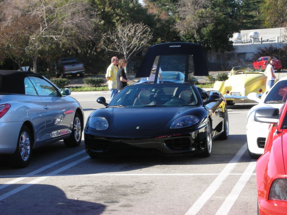Black Ferrari 360 Spider convertible parked in a lot between other sports cars