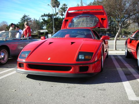 1998 Ford Crown Victoria - red Ferrari F40 sits with its large rear engine lid raised, parked among other cars at a sunny car meet.