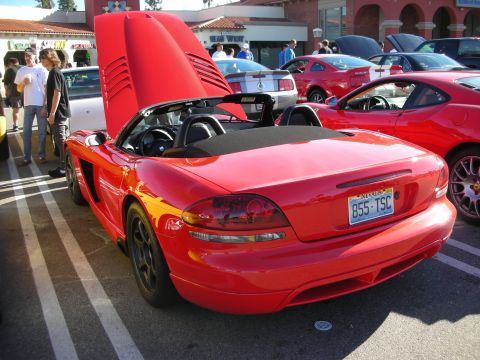 1998 Ford Crown Victoria - red Dodge Viper roadster with hardtop section raised sits rear-first among cars at an outdoor meet.