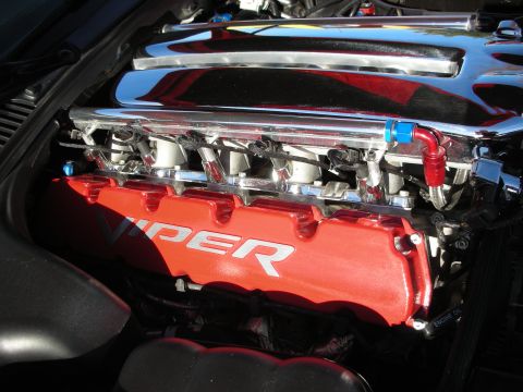 1998 Ford Crown Victoria - Close-up of a red engine valve cover stamped VIPER beneath chrome covers and braided fuel lines in an engine bay.