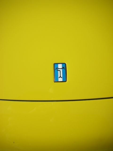 1998 Ford Crown Victoria - small blue-and-white enamel badge mounted on a glossy yellow car body panel above a body seam.