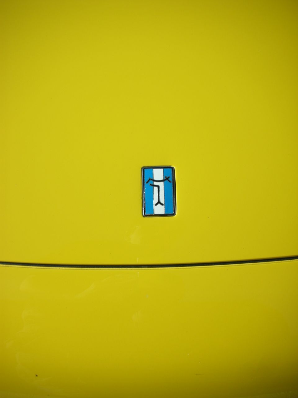 Blue and white enamel emblem on a glossy yellow car body panel