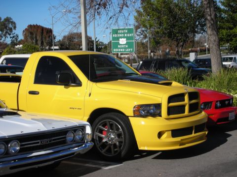1998 Ford Crown Victoria - Yellow Dodge Ram SRT-10 pickup with gray wheels parked beside other vehicles near green highway signs outdoors.
