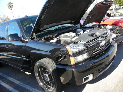 1998 Ford Crown Victoria - Black Chevrolet Silverado SS pickup with raised hood, chrome grille, and black-and-chrome wheels at an outdoor car meet.