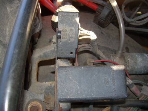 1988 Ford Bronco - Engine-bay close-up of a Ford self-test diagnostic connector cover molded "ELC TEST" with the Ford oval, hinged open above a dusty black co…