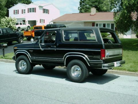 1984 Ford Bronco - A black Ford Bronco is parked on a residential street with other vehicles visible in the background.