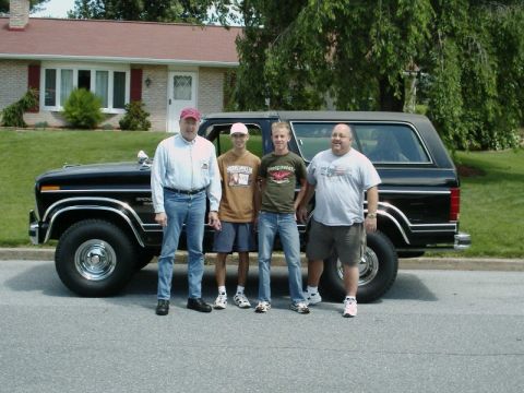 1984 Ford Bronco - Four individuals pose with a black Ford Bronco in front of a residential house.