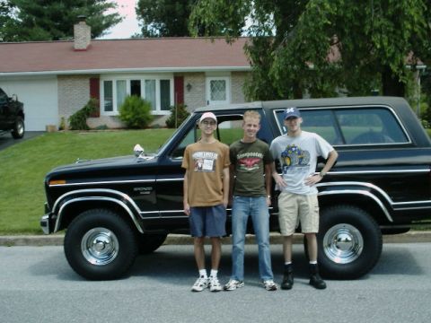 1984 Ford Bronco - Three young men pose with a classic black Ford Bronco in front of a suburban home.