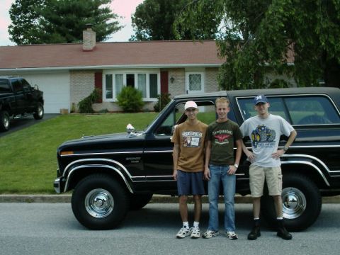 1984 Ford Bronco - A black Ford Bronco is parked in front of a house with three young men posing for a photo.