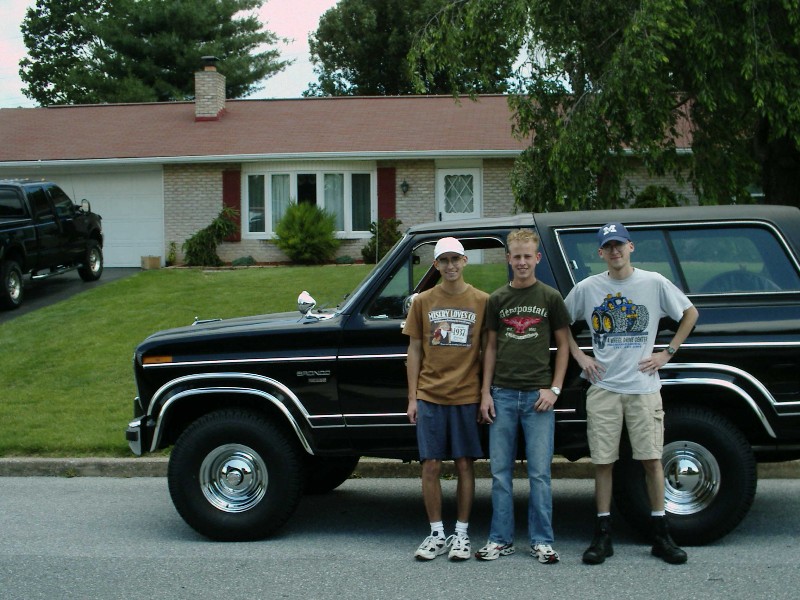 Black Ford Bronco with chrome trim and three young men standing in front of a suburban house