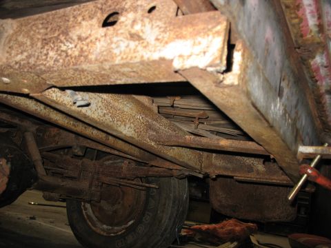 1952 Ford Pickup - The heavily rusted frame and leaf springs of a 1952 Ford Pickup are visible from the side.