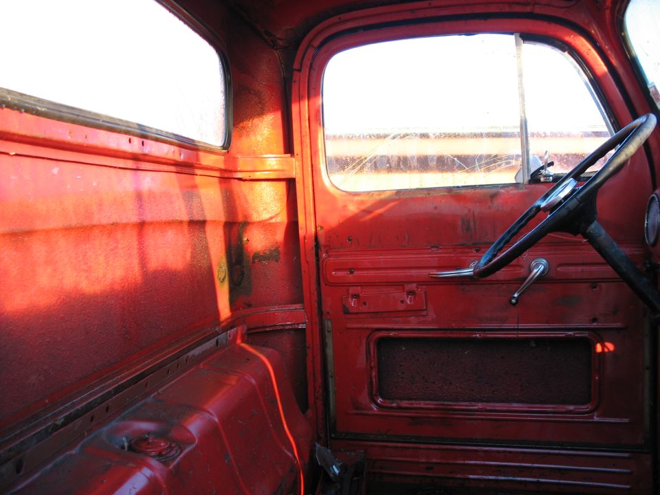Red truck interior showing door panel, steering wheel, and empty cab floor