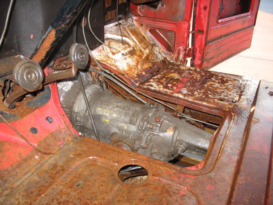 Interior view of a rusty truck floor with transmission visible