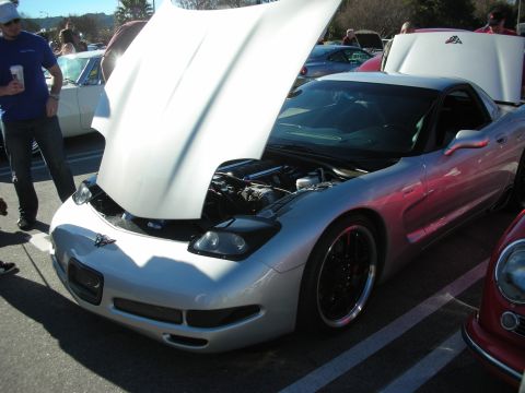 1998 Ford Crown Victoria - Silver C5 Corvette with its hood open showing the engine bay, parked among other cars at an outdoor event.