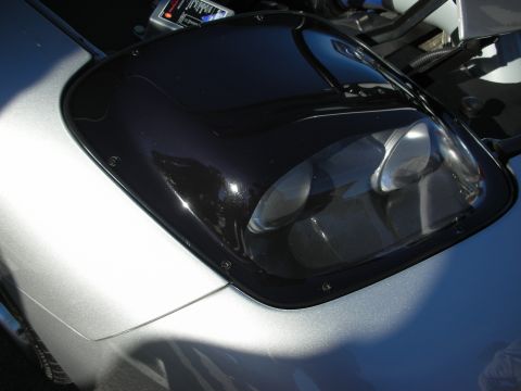 1998 Ford Crown Victoria - Close-up of a tinted black pop-up headlight assembly with projector lenses on a silver sports car body.