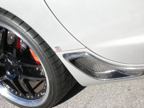 1998 Ford Crown Victoria - Detail of a polished multi-spoke wheel, red brake caliper, and carbon-fiber side intake vent on a silver sports car.