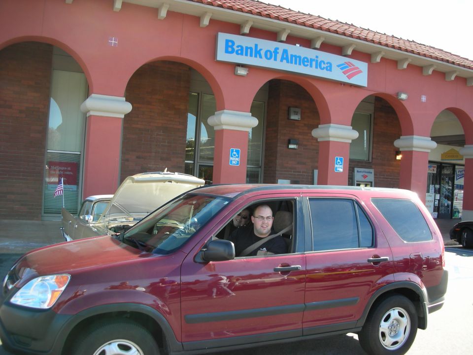 Man seated in a maroon Honda CR-V SUV parked outside a Bank of America