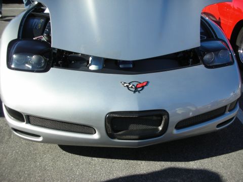 1998 Ford Crown Victoria - Silver C5 Corvette front end showing the crossed-flags emblem, mesh grilles, and exposed headlights at a car meet.