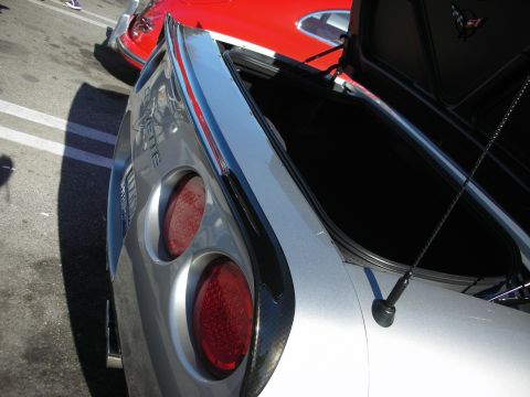 1998 Ford Crown Victoria - Detail of a silver Chevrolet Corvette's rear quarter panel with twin round taillights and raised rear hatch at a car show.