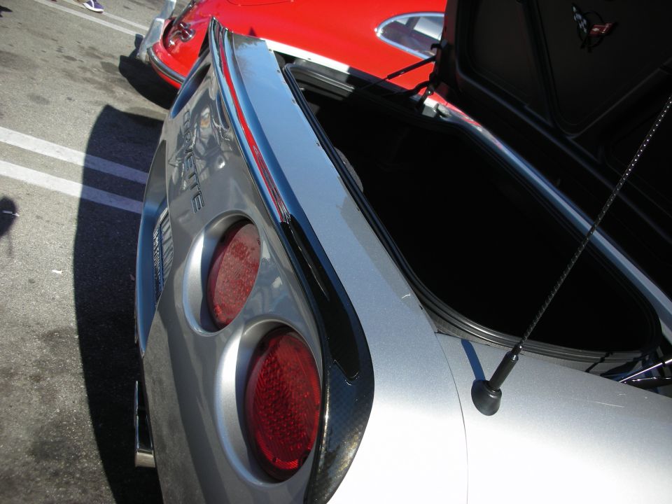 Close-up of a silver Corvette rear quarter showing twin round taillights and 'CORVETTE' badge with open trunk