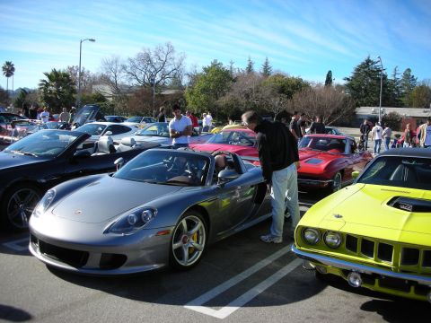 1998 Ford Crown Victoria - silver Porsche Carrera GT parked next to a bright green classic muscle car among a row of sports cars at an outdoor meet.