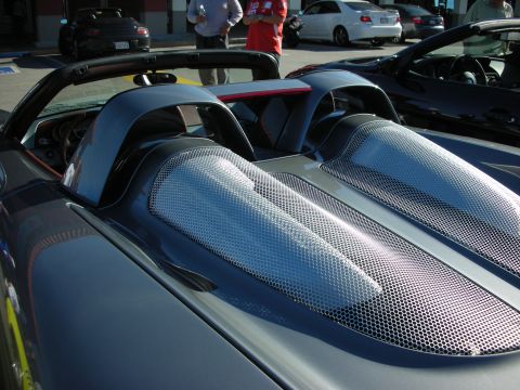 1998 Ford Crown Victoria - Close-up of the rear deck and mesh engine-cover vents of a dark mid-engine convertible sports car in a sunny parking lot.