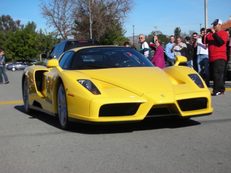 Yellow Ferrari Enzo front three-quarter being driven past a crowd of onlookers