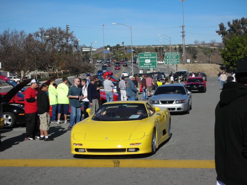 Yellow wedge-shaped exotic sports car front view amid a crowd at an outdoor car meet