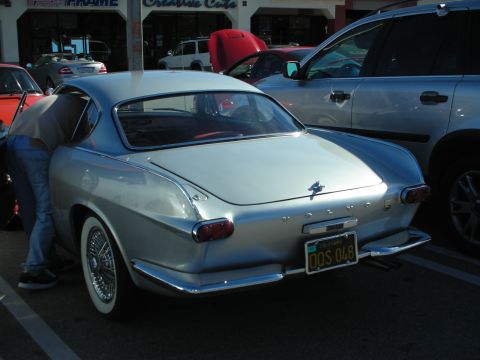 1998 Ford Crown Victoria - silver Volvo P1800 coupe with chrome wire wheels and red interior shown rear three-quarter in a shopping-center lot.