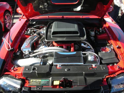 1998 Ford Crown Victoria - engine bay of a red car showing a black air-box, polished supercharger piping and a Vortech-labeled blower under an open hood.