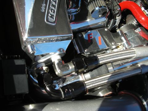1998 Ford Crown Victoria - Tight close-up of polished engine plumbing, braided stainless lines and a chromed valve cover with an 'F1' marking.