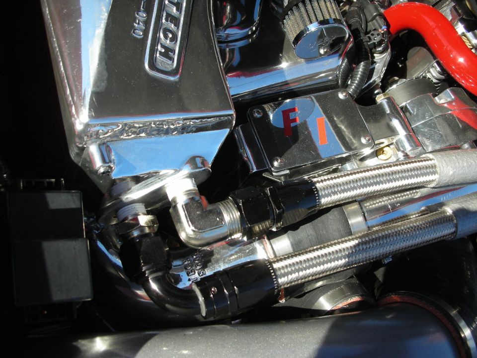 Close-up of polished engine components, braided steel lines and a chromed valve cover