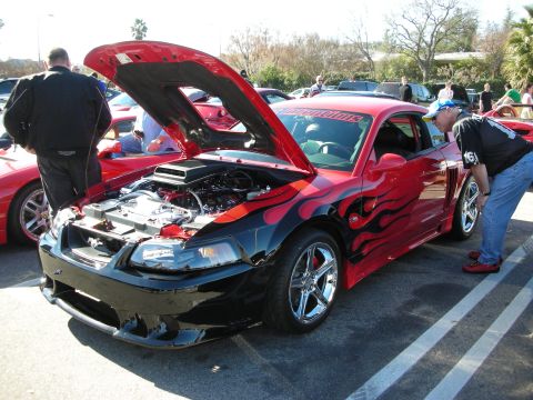 1998 Ford Crown Victoria - red and black flame-painted Ford Mustang shown with its hood up displaying the engine among spectators at an outdoor meet.