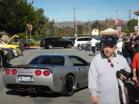 1998 Ford Crown Victoria - silver Chevrolet Corvette shown rear three-quarter in a car-show lot as a man with a Canon camera stands in the foreground.