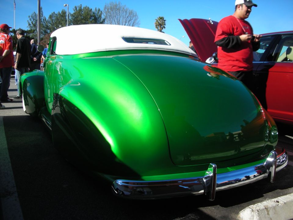 Rear three-quarter view of a green custom lead-sled coupe with white convertible top at a car show