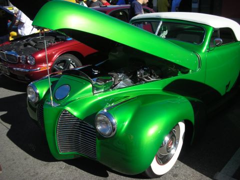 1998 Ford Crown Victoria - candy-green custom coupe with hood raised reveals its engine, riding on wide whitewall tires beside a maroon sedan.