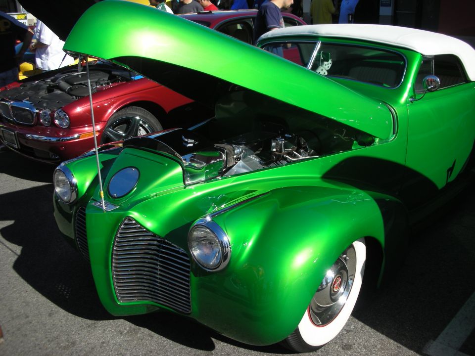 Front of a green custom coupe with open hood showing engine, white top, wide whitewall tires