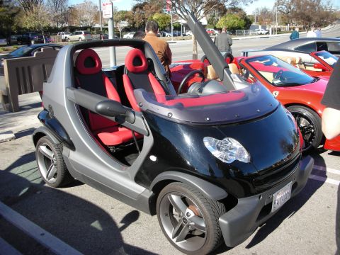 1998 Ford Crown Victoria - two-seat black-and-silver Smart roadster with red bucket seats parked at an outdoor car meet.