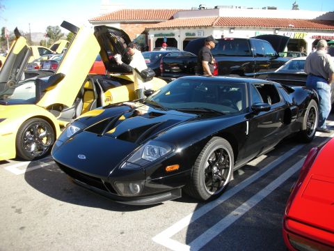 1998 Ford Crown Victoria - black Ford GT supercar sits in a parking lot next to a yellow exotic with its door raised.