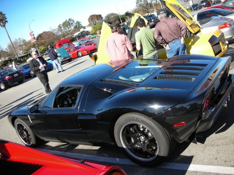 1998 Ford Crown Victoria - Looking down at a black Ford GT's engine cover and side, parked in a busy lot with spectators and supercars.