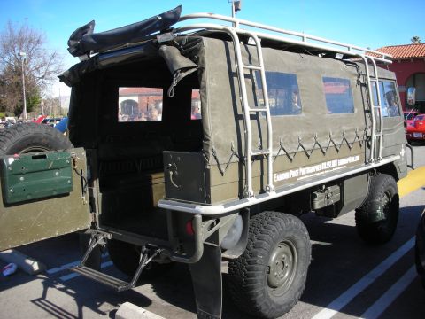 1998 Ford Crown Victoria - Rear three-quarter of an olive-drab military truck with canvas-covered bed, roof rack, ladder and spare tire.