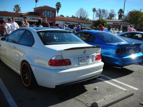 1998 Ford Crown Victoria - white BMW M3 coupe with carbon spoiler and orange-rimmed wheels parked next to a blue BMW in a busy lot.