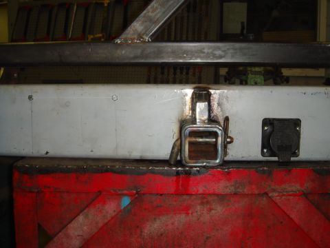 1996 Ford Bronco - Close-up of a trailer hitch receiver and an electrical outlet mounted on a vehicle bumper.