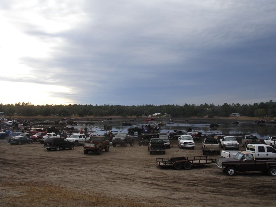Muddy field with numerous trucks and SUVs gathered under a cloudy sky