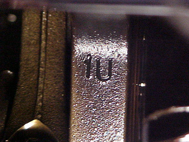 Close-up of a dark metal engine part with raised markings '1U' and a watermark 'SUPERMOTORS'