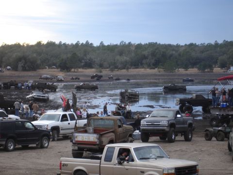 1989 Ford Bronco - A muddy field is filled with trucks and people enjoying an outdoor event.