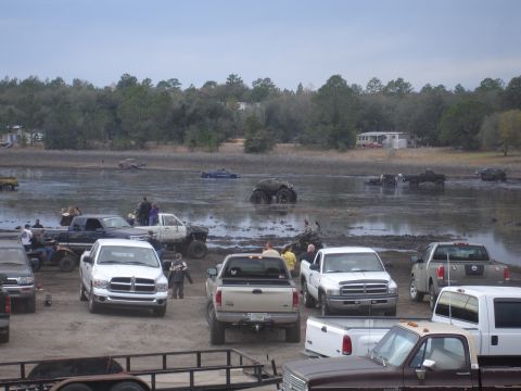 1989 Ford Bronco - A muddy field is filled with trucks and ATVs, with some vehicles stuck in the mire.